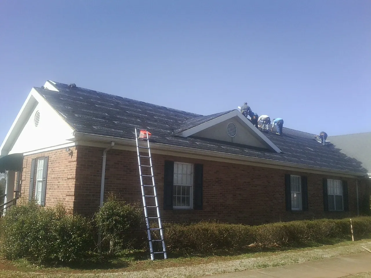 Crew tearing shingles off a brick ranch roof with a ladder set — Emergency Roof Repair work by our crew in Alpine