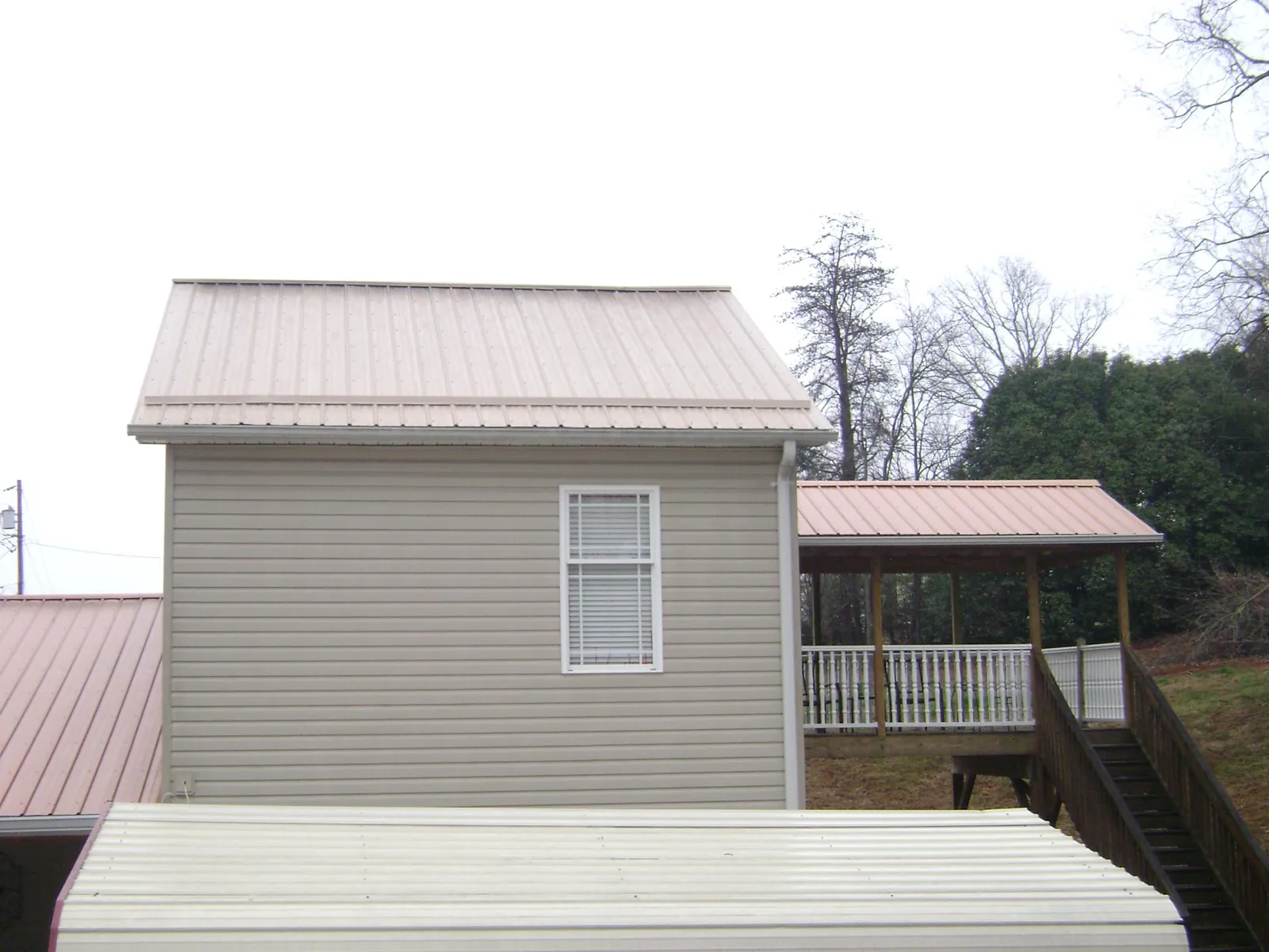 Tan metal roofs on a two story addition and attached porch, from a Roof Replacement job in Alpine